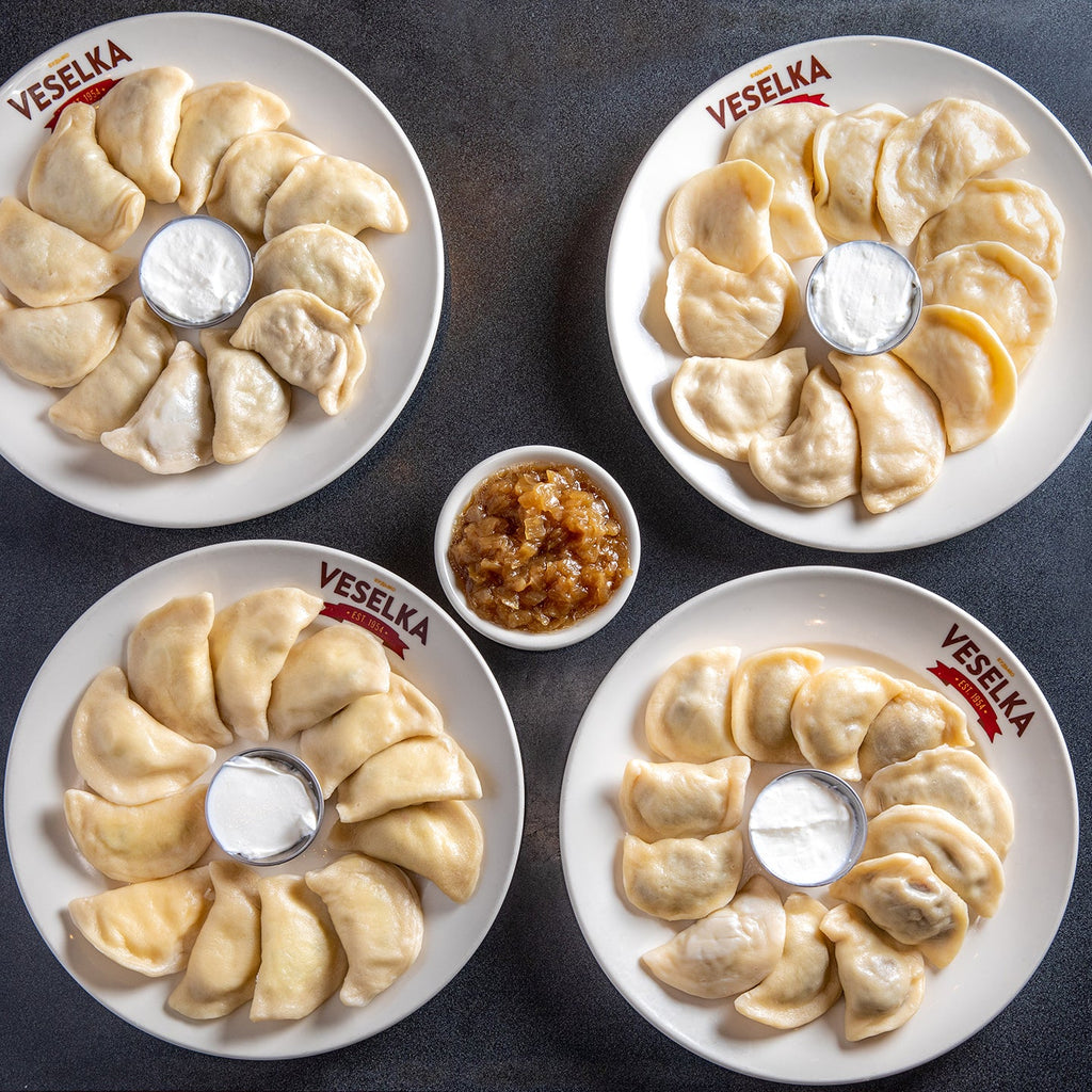 Four dozen pierogi on plates, top down shot, pierogi are boiled, and fried onions on the side